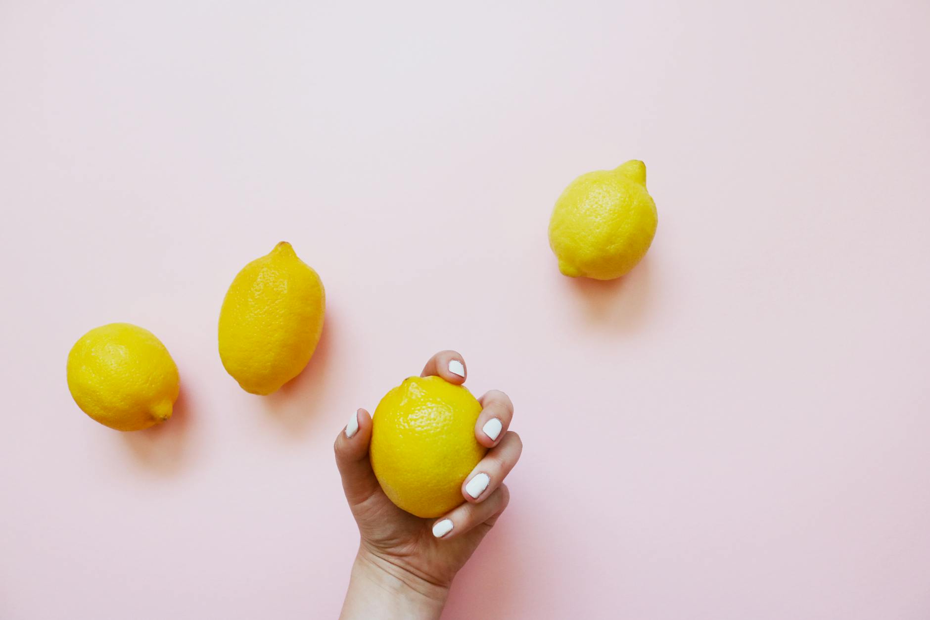 A hand holding a fresh lemon on a soft pink background, symbolizing gentle, natural pleasure