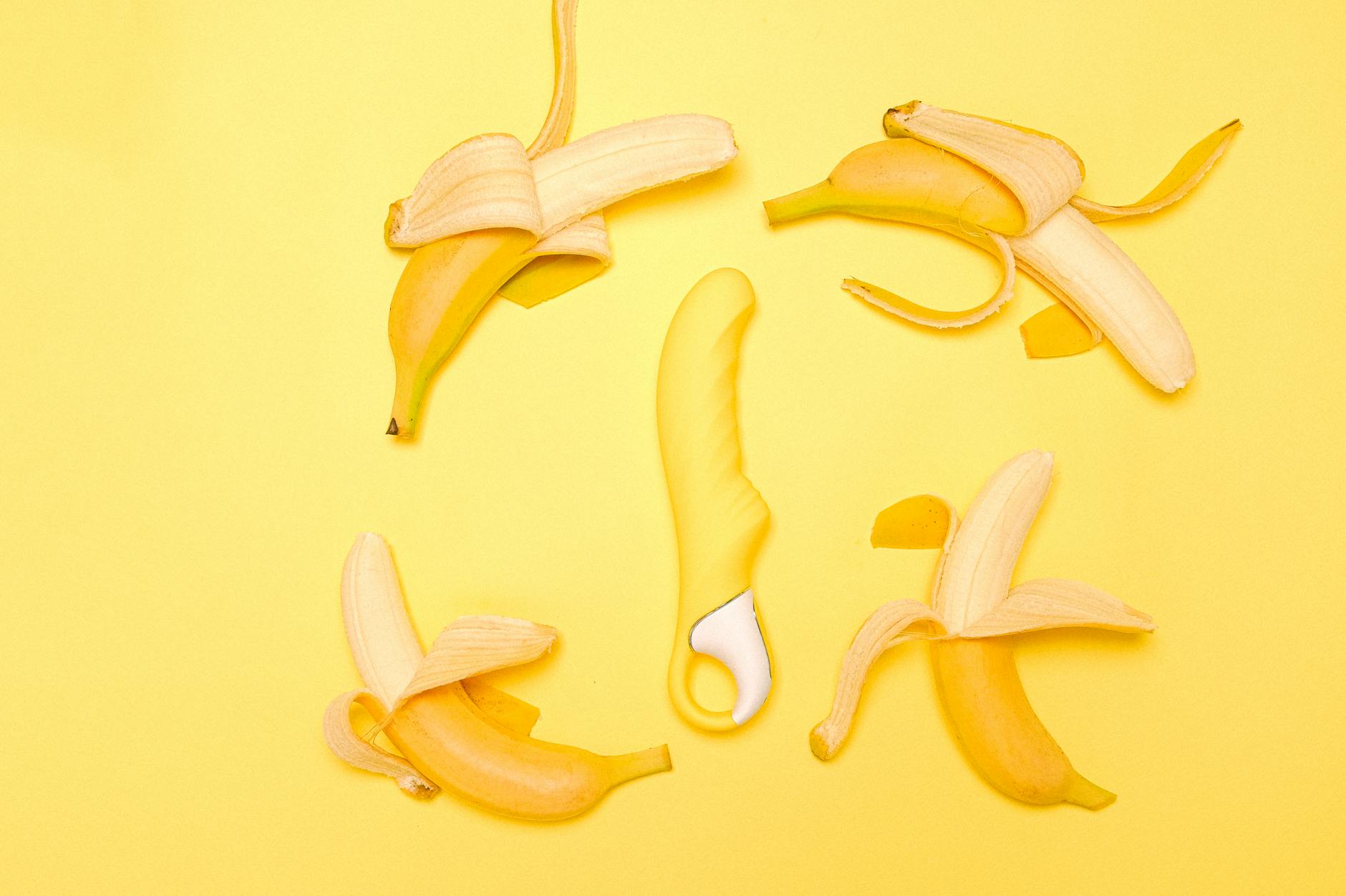 Yellow silicone lemon vibrator surrounded by peeled bananas on a yellow background