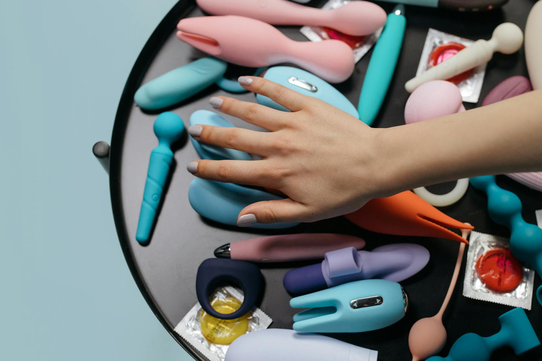 Hands arranging colorful vibrators on a surface, representing choice and exploration without judgment