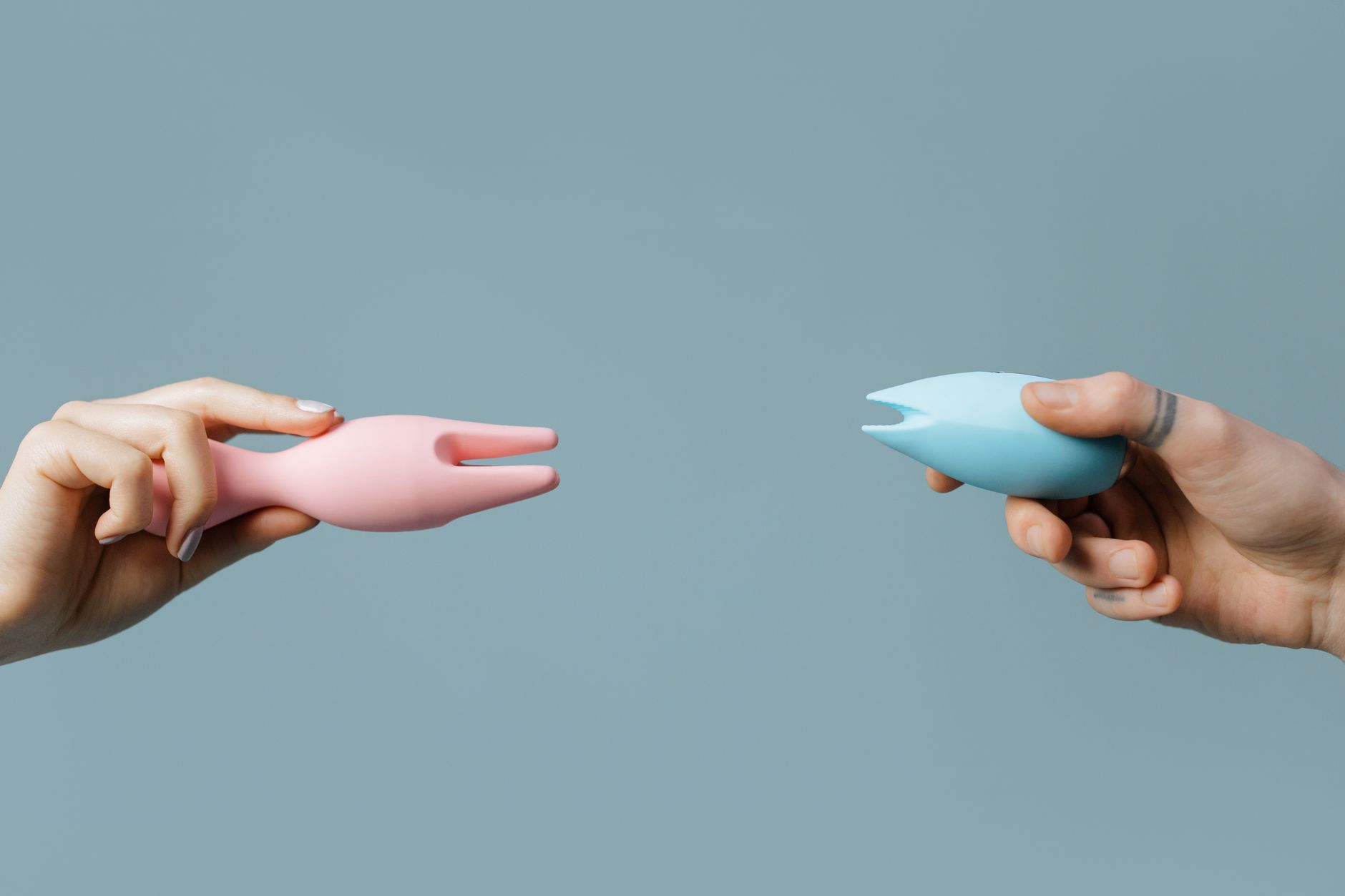 Close-up of a hand holding an orange vibrator against a minimalistic purple backdrop