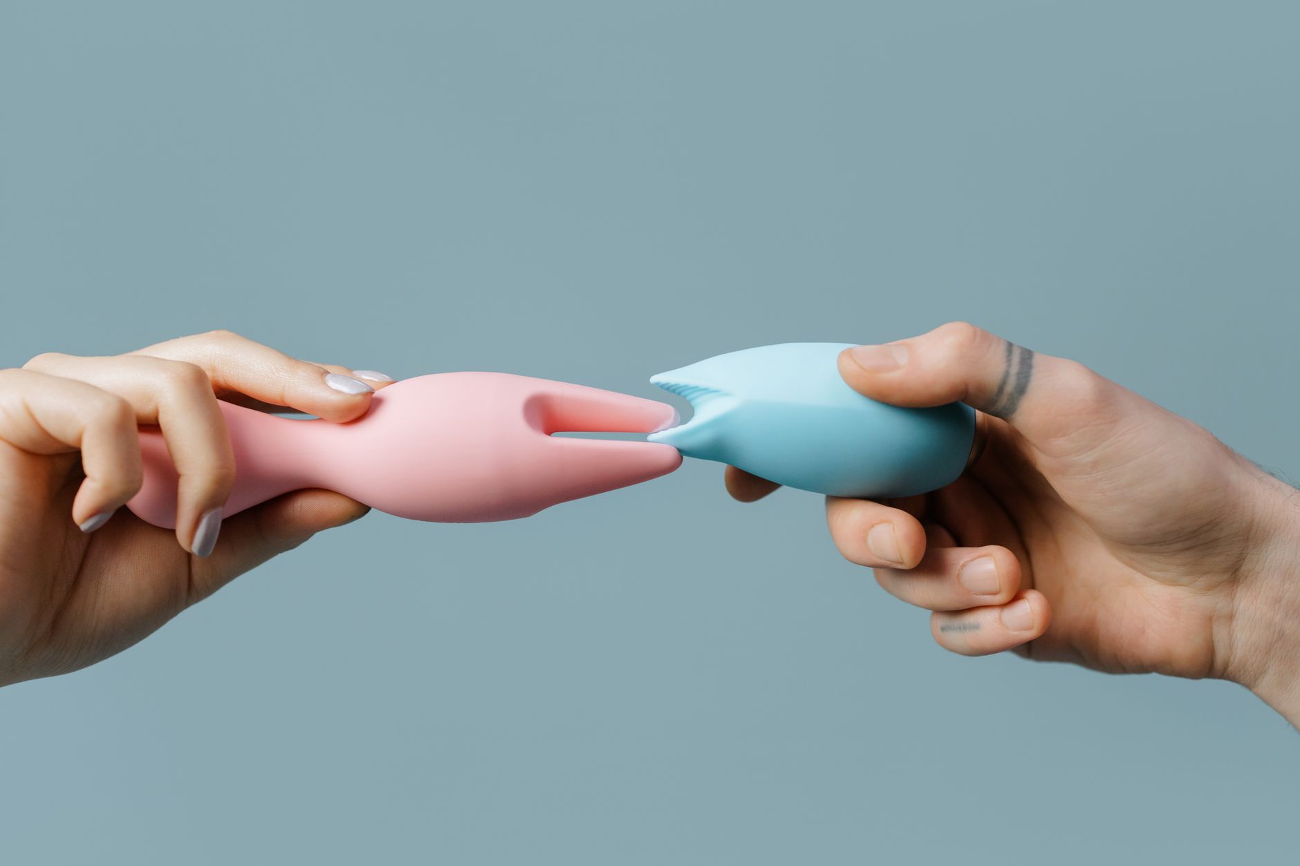 Two hands holding pastel-colored silicone vibrators together, symbolizing intimate connection and shared pleasure.