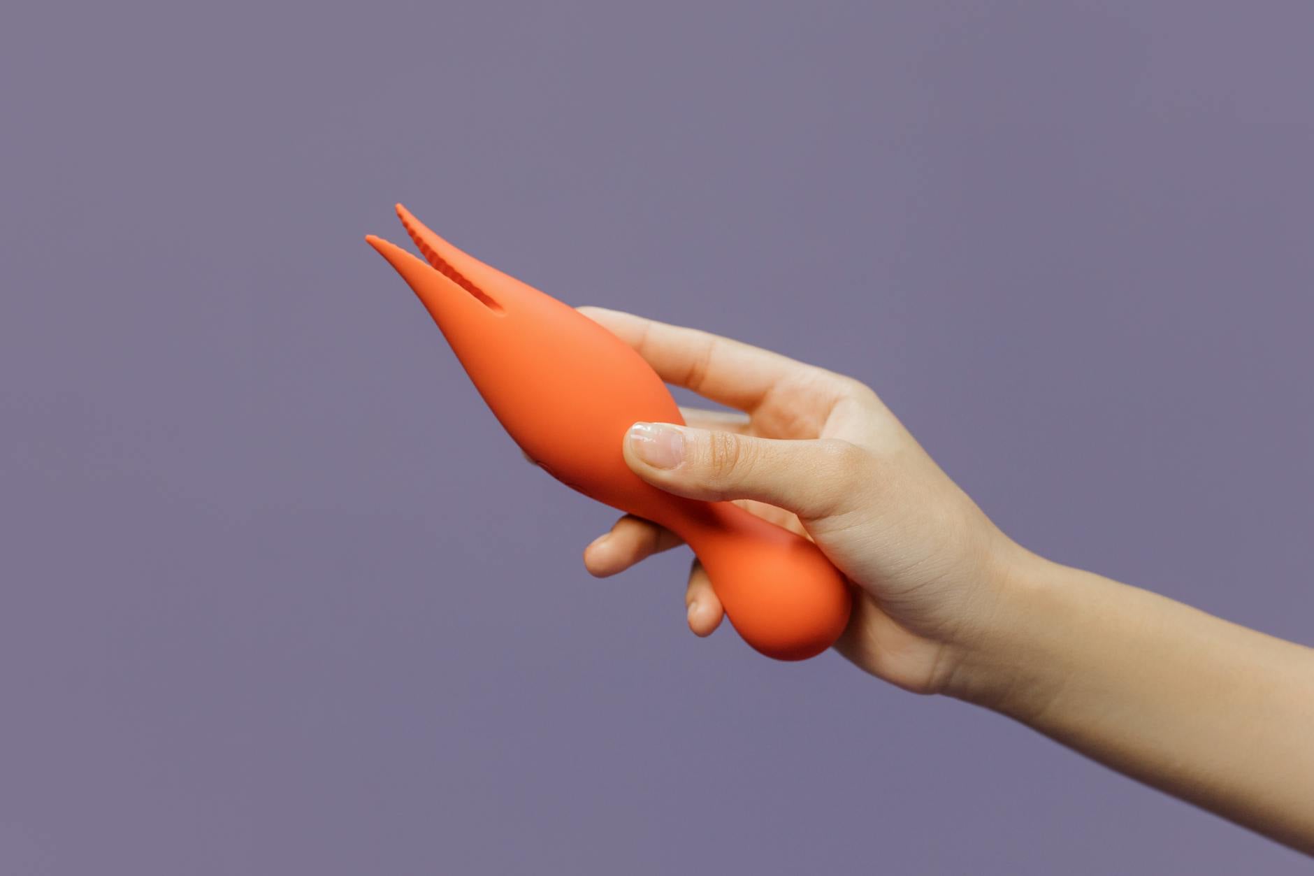 Hand holding a vibrator against a minimalist backdrop, representing modern pleasure tools