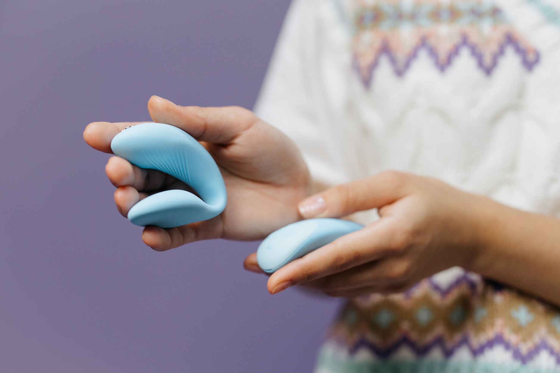 Close-up hands holding a sleek personal vibrator against a purple background.