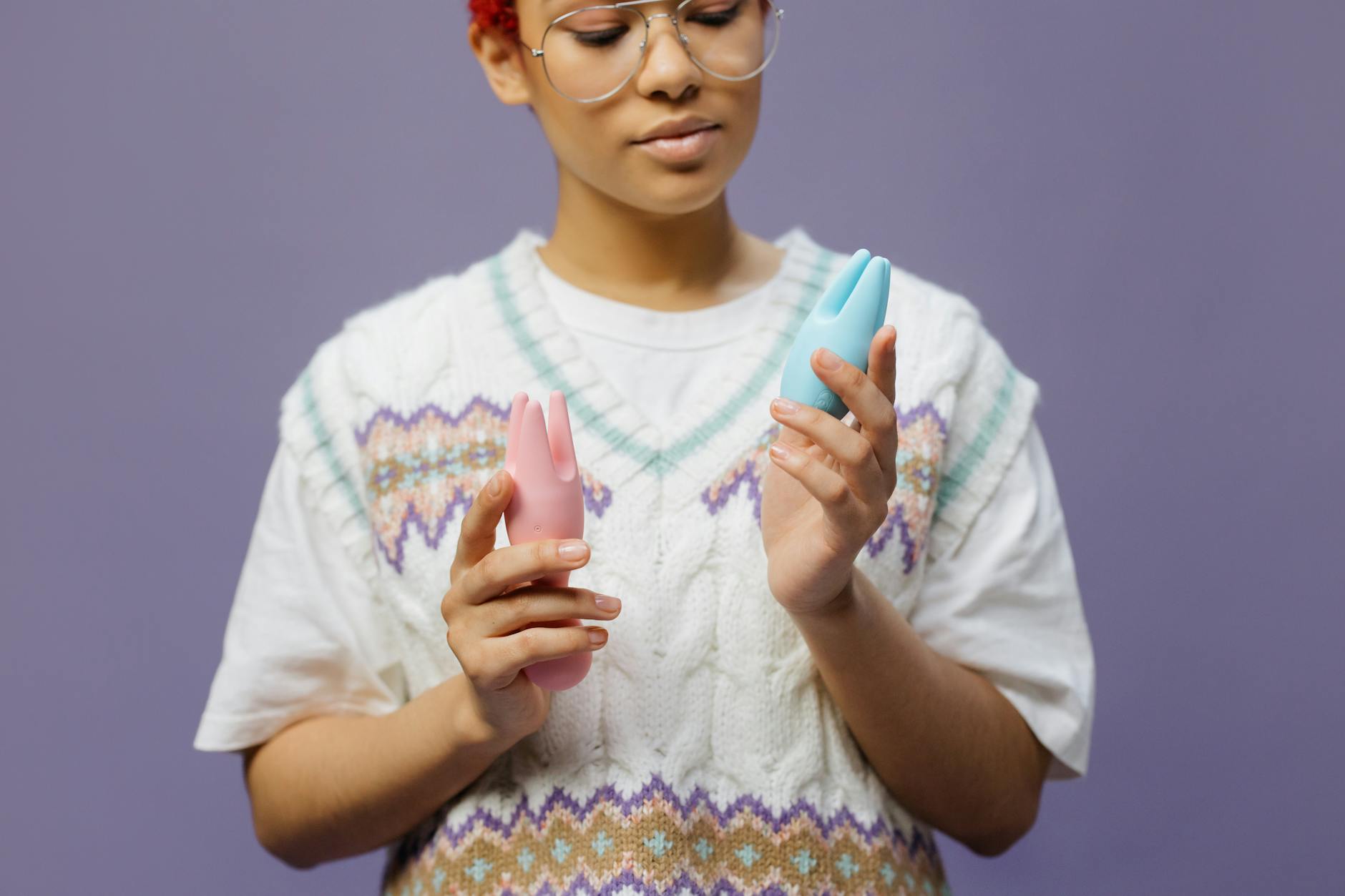 Woman holding blue and pink vibrators thoughtfully against a soft background